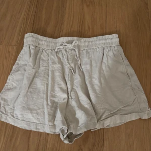 Beiga linneshorts från Zara med snörning - Luftiga beiga shorts från Zara i storlek L, tillverkade i linne. De har elastisk midja med snörning och fickor i sidorna. Perfekta för varma dagar när du vill ha en chill och avslappnad stil.  