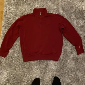 Röd half zip tröja från Champion - Säljer en snygg vinröd långärmad tröja från Champion med half zip och hög krage. Tröjan har broderad logga på bröstet och ärmarna, samt två fickor. 