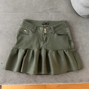 Lågmidjad militärgrön jeanskjol med volanger - Säljer en militärgrön jeanskjol med volanger som är lågmidjad. Midjemått 37 cm, längd fram 33 cm, längd bak 39 cm. Har sytt den själv väldigt noga 💚 