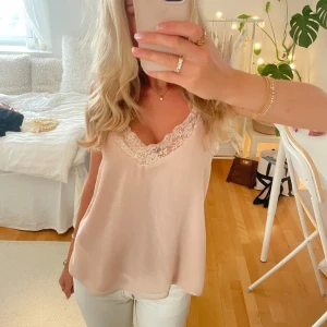 Ljusrosa linnetopp med spets - Supersöt ljusrosa linnetopp med v-ringning och fina spetsdetaljer längs urringningen. Tunt och flowy material som känns luftigt och fräscht. Perfekt att styla med jeans eller kjol för en chill och feminin look.