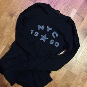 Svart långärmad tröja NYC 1990 Urban Outfitters - Svart långärmad tröja från Urban Outfitters med  NYC 1990-tryck och stjärna framtill 