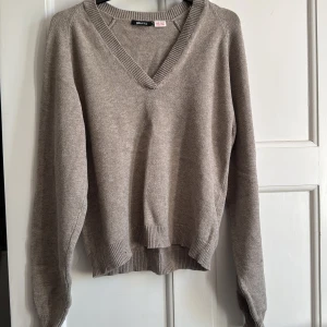 Beige v-ringad stickad tröja Gina Tricot - Beige stickad tröja från Gina Tricot i storlek S. Tröjan har v-ringning, ribbade muddar och lång ärm. Perfekt för lager-på-lager och enkel att matcha med jeans eller kjol. Mjuk och skön känsla, passar dig som gillar en clean och stilren look.