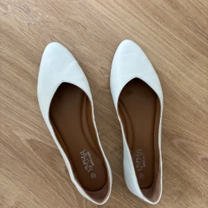 Vita ballerinaskor från Emma - Snygga vita ballerinaskor från Emma med spetsig tå och platt sula. Skorna är gjorda i mjukt skinn och har en stilren, minimalistisk design som passar perfekt till många olika outfits.