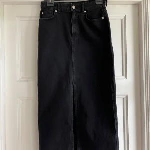 Stockholm studio svart lång jeanskjol med slits från  - Svart långkjol i jeansmaterial med klassiska fickor fram och bak. Kjolen har en rak passform och en snygg slits framtill. 