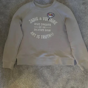 Beige tröja från Zadig & Voltaire - Säljer en beige tröja från Zadig & Voltaire med texten 'Art is Truth' och ett färgglatt märke längst upp. Tröjan har långa ärmar och rund halsringning. Perfekt för en avslappnad stil.