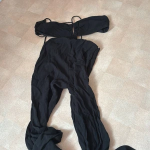 Svart offshoulder jumpsuit H&M - Supersnygg svart jumpsuit från H&M med offshoulder och smala axelband. Vida ben och rynkade detaljer upptill ger en trendig look. Perfekt för dig som vill sticka ut med en cool och stilren outfit.