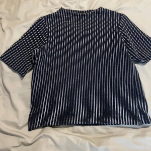 Randig t-shirt från Lindex, marinblå - Snygg marinblå t-shirt från Lindex i storlek M med vita ränder i ett coolt mönster. T-shirten har korta ärmar och en rak passform. Perfekt för dig som gillar en stilren men ändå unik look.