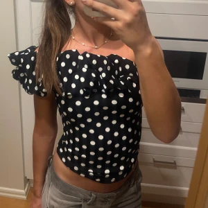 Svart prickig offshoulder topp - Superfin prickig offshoulder topp med volang upptill, går att ha både one shoulder och off shoulder💗 Helt nytt skick!