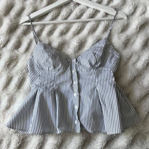Randig topp från Zara - Byter gärna mot liknande/likadan i M!! Superfin eftertraktad randig topp från Zara med smala axelband och knappar framtill. Toppen har en figurnära passform upptill och utsvängd nertill, samt markerade kupor för en snygg siluett. Perfekt till jeans eller kjol för en fräsch look. Säljer pga för liten , storlek S, kom gärna med prisförslag