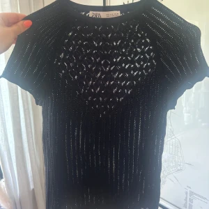 Svart stickad topp från Zara - Snygg svart stickad topp från Zara med korta ärmar och rund hals. Toppen har ett genombrutet mönster med coola detaljer och vågig kant nertill. Perfekt att styla med jeans eller kjol beroende på vart du ska!! 🖤