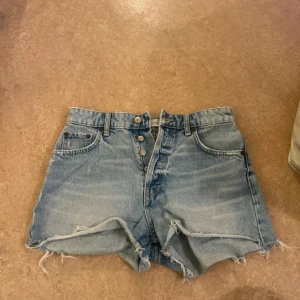 Ljusblå jeansshorts från Zara - Snygga jeansshorts i ljusblå denim med råa, fransiga kanter och klassiska fem fickor. Knappar framtill och bälteshällor. Perfekta för sommaren och ger en avslappnad vibe till din outfit.