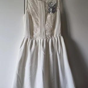 Vit spetsklänning från Zara Trafaluc - Supersöt vit kortklänning från Zara Trafaluc i storlek S. Klänningen har ärmlös design, spetsdetaljer upptill och veckad kjol. Framsidan har dekorativa veck och spetsmönster som ger en romantisk vibe. Perfekt för sommarens alla tillfällen!