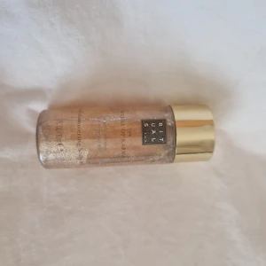 Rituals The Ritual of Karma Shimmering Body Mist - Glittrig face mist från Rituals i serien The Ritual of Karma. Kommer i en genomskinlig flaska med guldigt lock och innehåller skimrande guldpartiklar som ger huden en fräsch glow. Perfekt för att fräscha upp ansiktet och ge extra lyster.