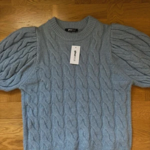 Blå stickad tröja med puffärm Gina Tricot - Supersöt ljusblå stickad tröja från Gina Tricot med puffiga kortärmar och grovt kabelstickat mönster. Rund halsringning med ribbad kant och mjukt material som känns skönt mot huden. Perfekt för dig som vill ha en chill men ändå stylish look.