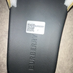 Burberry sandaler med klassiskt rutmönster - Snygga sandaler från Burberry med svart sula och klassiskt beige rutmönster på remmen. Tillverkade i Italien med präglad Burberry-logga på sulan. Perfekta för sommaren och ger en lyxig vibe till din outfit.