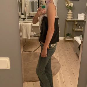 Svart axelväska med kedja Gina Tricot - Cool svart axelväska från Gina Tricot med silverfärgade kedjor längs sidorna och som axelrem. Väskan har en mjuk, lite slouchy form och är tillverkad i syntetmaterial som ger en skinnliknande känsla. Perfekt storlek för att få plats med allt du behöver.