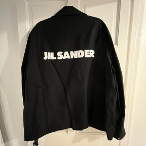 Jil Sander Jacka - Svart vindjacka från Jil Sander i super bra skick. Passar dig som brukar bära stl L, Tagsen sitter inte på längre