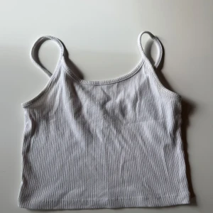 Vit ribbad linnetopp från Sister - En enkel och fräsch vit ribbad linnetopp från Sister. Toppen har smala axelband och är croppad i modellen, perfekt till jeans eller kjol. Materialet är mjukt och stretchigt, vilket gör den superbekväm att bära hela dagen.