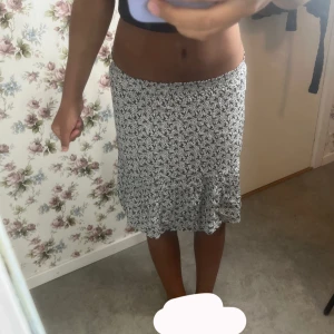 Svartvit blommig kjol med volang - Supersöt svartvit blommig kjol med volangkant nertill. Kjolen har en lätt utsvängd form och sitter skönt i midjan. Perfekt för dig som gillar en feminin och trendig stil.