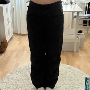 Svarta parachute pants från Bershka - Svarta parachute pants från Bershka med dragsko i midjan och vid benslut. Byxorna har en loose passform och är tillverkade i jeansaktigt material. 