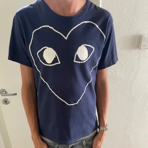 Blå t-shirt Comme des Garçons Play  - Tjenare, säljer denna fräscha mörkblå t-shirt från Comme des Garçons Play med stort vitt hjärta och ögon tryckt på framsidan. Storlek: S 9/10 skick. Ny pris 1200kr. Mitt pris 499kr. Modellen är 181 cm och väger ungefär 60 kg. Tveka inte på att höra av er! Mvh ville 