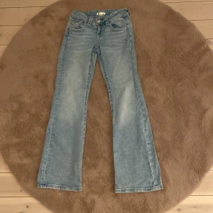 Bootcut jeans från Gina Tricot, ljusblå - Ljusblå bootcut jeans från Gina Tricot i storlek 152. Klassisk femficksmodell med dragkedja och knapp framtill. Jeansen har en snygg tvättad look och är tillverkade i mjukt denimtyg. Perfekta för en avslappnad och trendig stil.