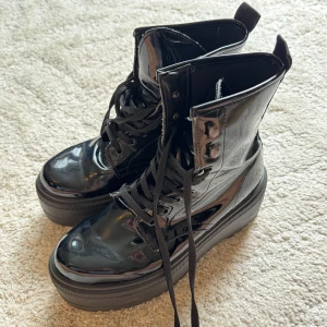 Svarta lackade boots med platåsula - Snygga svarta boots i lackad finish med kraftig platåsula och snörning framtill. Skorna har rund tå och grov yttersula för extra edge. Tillverkade i Italien och perfekta för dig som vill sticka ut med en cool och modern look.