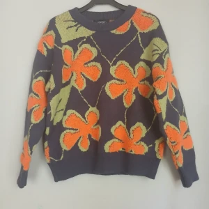  Äkta 70-talsretro – Cider stickad blommig tröja i färgexplosion – strl S  - Flower power i stickad form – unik 70-talsretro som värmer & väcker uppmärksamhet!  Direkt från flower power-erans färgstarka garderober! Den här stickade tröjan från Cider är som hämtad ur ett 70-talsmode-magasin – med stora orangea blomblad och frodiga gröna blad på en djup marinblå botten. Ett statement-plagg som för tankarna till varma höstdagar, skivspelare som snurrar och doften av nybryggt kaffe i ett bohemiskt kök.  Storlek: S  Skick: fint skick   Stil: 70-tal, boho, flower power, retro