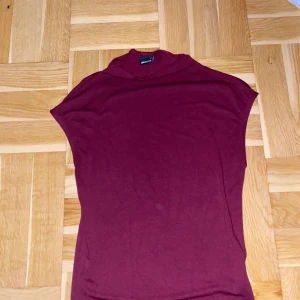 Vinröd polotopp från Gina Tricot - Vinröd polotopp från Gina Tricot i mjukt material. Toppen har en hög krage och är ärmlös 