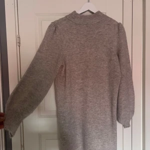 Grå stickad klänning från JDY - Mysig gråmelerad stickad klänning från JDY med hög hals och långa ärmar. Modellen är rak och har ribbade muddar vid ärmslut och nederkant. Perfekt för dig som gillar enkelt.