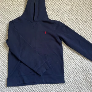 Mörkblå hoodie från Polo Ralph Lauren - Snygg mörkblå hoodie från Polo Ralph Lauren i storlek S. Tröjan har en klassisk huva, magficka och det ikoniska röda Polo-broderiet på bröstet. Tillverkad i mjuk bomull, perfekt för chill dagar och streetwear-stil. Den är bara använd några få gånger.💓 Hör av er om ni vill ha fler bilder eller har några frågor!