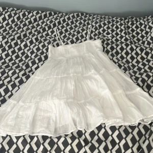 Vit somrig kortklänning Gina Tricot - Supersöt vit klänning från Gina Tricot med tunna axelband och volangkjol. Smockad upptill och luftig i bomull, perfekt för varma dagar. Den har en flowy passform och ärmlös design som ger en fräsch och chill vibe.