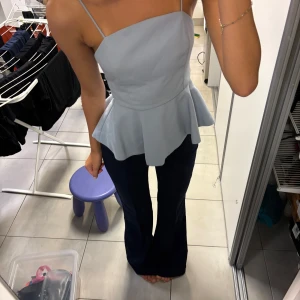 Ljusblå peplum linne med rosett - Supersöt ljusblå linne med peplumvolang och smala axelband. Toppen har en stor rosett baktill och dragkedja i ryggen. 