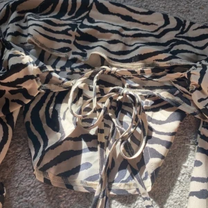 Zebramönstrad omlottopp från SHEIN - Snygg omlottopp från SHEIN i beige och svart zebramönster. Toppen har långa band för knytning i ryggen och croppad passform.