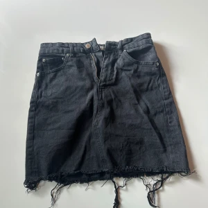 Svart jeanskjol med fransad kant - Cool svart jeanskjol från g perfect jeans i storlek 34. Kjolen har klassiska fickor fram och bak, dragkedja och knapp i midjan. Den är kort och har en rå, fransad kant nedtill som ger en edgy vibe. Perfekt för dig som gillar streetstyle.