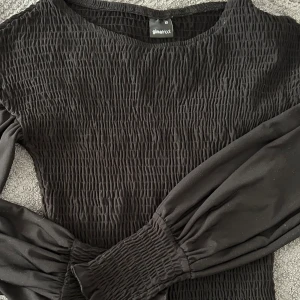 Svart smockad topp från Gina Tricot - Säljer en svart topp från Gina Tricot med smockdetaljer och långa ärmar. Toppen har en elastisk passform och är perfekt för en stilren look. Passar bra till både jeans och kjol. Säljer pga inte min stil. Använd fåtal gånger.❤️storlek xs