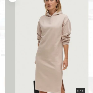 Beige hoodieklänning  - Hoodieklänning i fin beige färg med lång ärm och huva. Klänningen har en rak passform och slits på sidan och mycket skönt material. 
