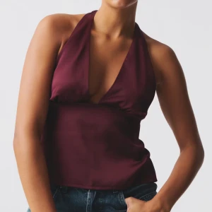 Vinröd halterneck topp med knyt - Säljer en vinröd halterneck topp i glansigt material med djup v-ringning och öppen rygg. Har använt vid endast ett tillfälle så i super bra skick. Nypris 360kr