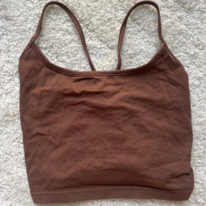 Brun croppad linne - Snygg brun croppat linnemed smala axelband och knytning i ryggen. Toppen är ärmlös och har en enkel, stilren design som passar perfekt till jeans eller kjol. Mjuk bomullskänsla och lätt stretch för skön passform.