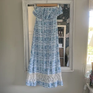 Blå långklänning från Abercrombie - Säljer en superfin blå långklänning från Abercrombie med offshoulder och smock upptill. Klänningen har ett mönster i olika blå nyanser och vit spetsdetalj längst ner. Materialet känns lätt och luftigt, perfekt för varma dagar. 