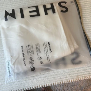 Vit långkjol med slits från SHEIN - Snygg vit långkjol från SHEIN i jeansmaterial med rak passform och en cool slits framtill. Kjolen har en enkel design utan mönster och passar perfekt till sneakers eller boots. Fräscht och stilrent plagg för dig som gillar minimalistisk vibe.