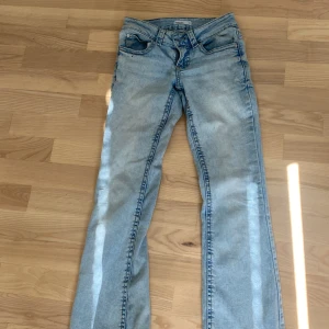 Ljusblå bootcut jeans låg midja - Säljer ett par ljusblå jeans med bootcut passform och låg midja. Jeansen har klassiska fem fickor, snygga slitningar vid benslut och är tillverkade i mjukt denimtyg. Perfekta för dig som gillar en avslappnad och trendig look.
