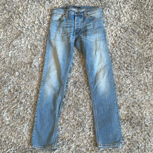 Blå jeans från Nudie Jeans, 30/32 - Snygga ljusblå jeans från Nudie Jeans i klassisk straight fit. Jeansen har fem fickor, orangea sömmar och en cool tvättad look. Perfekt passform med normal midja och raka ben. Materialet är slitstarkt denim i bomull.
