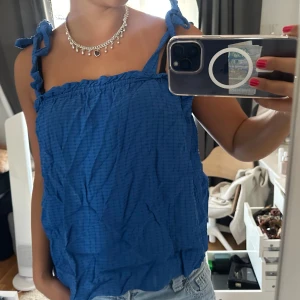 Blå linnetopp med knytband - Snygg blå linnetopp med knytband på axlarna och lätt strukturerat tyg. Perfekt för varma dagar och enkel att styla med jeans eller kjol. Luftig och bekväm passform med ärmlös design.