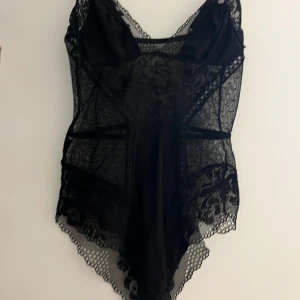 Svart spetskorsett - Elegant svart korsett med vacker spetsdetaljering. Den har en figurnära passform och är perfekt för att ge en stilfull look. Spetsen ger en lyxig känsla och den är designad för att framhäva silhuetten.