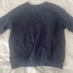 Mörkblå sweatshirt med USA-tryck - Säljer en mörkblå sweatshirt med texten 'USA' och en liten amerikansk flagga på framsidan. Tröjan har långa ärmar och en rund halsringning. Perfekt för en avslappnad stil.