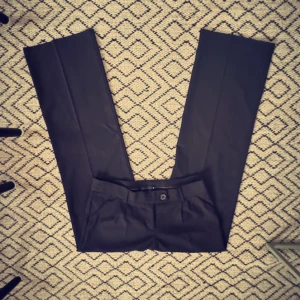 Svarta kostymbyxor Vero Moda  - Snygga lowwaist kostymbyxor från Vero Moda med en klassisk design. De är svarta med smala ränder. De har en knapp och dragkedja framtill, fickor, samt hällor för bälte. Perfekta för en stilren look. Raka i modellen. 