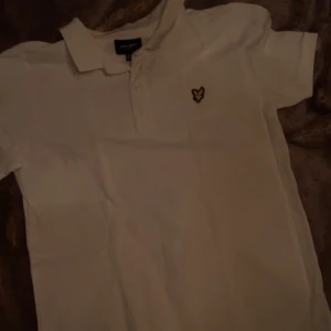 Vit pikétröja från Lyle & Scott - Säljer en klassisk vit pikétröja från Lyle & Scott med korta ärmar och en liten broderad logotyp på bröstet. Perfekt för en stilren och avslappnad look.