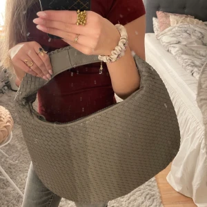 Beige flätad axelväska - Säljer en snygg trendig grå axelväska med flätat mönster. Väskan har en praktisk dragkedja och ett rymligt inre fack. Perfekt för att bära med sig det viktigaste med stil. Den är ganska stor så man får plats med mycket!💓 aldrig använt