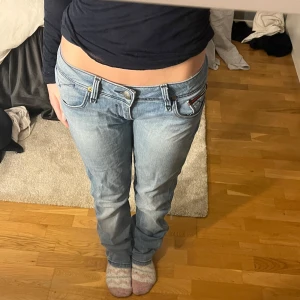 Ljusblå jeans med låg midja - Snygga ljusblå jeans med låg midja och klassisk femficksdesign. De har en knapp och dragkedja framtill samt subtila slitningar för en trendig look. Perfekta för en avslappnad stil. Säljer för att de är förstora för mig💗